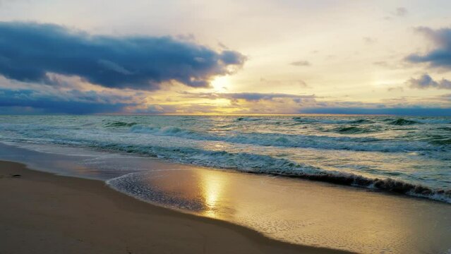 Beautiful sunset on seashore. Picturesque sunrise on deserted ocean shore. Sea waves roll on sandy coast. Relaxing view of marine landswell. Summer seascape. Paradise beach in morning or evening