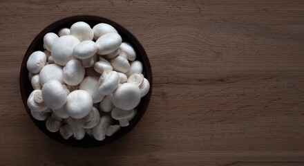 Fresh white mushrooms in a bowl on a wooden table top view.