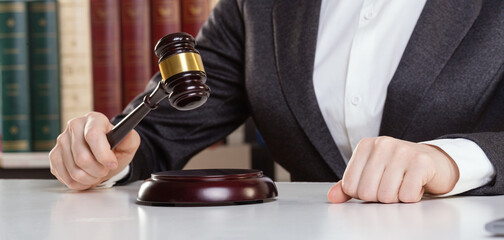 Female hands in formal wear with maroon auction gavel on a desk surface in an office, selected focus.