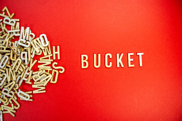 Fototapeta na wymiar BUCKET in wooden English words language capital letters spilling from a pile of letters on a red background