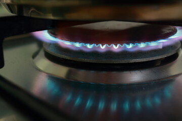 Close-up view on propane butane fuel (LPG or petroleum gas) kitchen stove (hob) with blue flame and metal cooking pot.