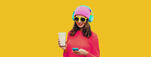 Portrait of modern young woman in wireless headphones listening to music with smartphone wearing...