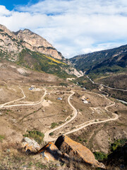 Mountain serpentine in sunlight. Dangerous narrow dirt mountain road through the hills to a high-altitude village. Vertical view.