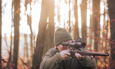 Autumn hunting season, hunter with rifle looking out for some wild animal in a wood or forest,...