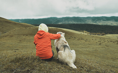 Female hiker sitting with dog outdoors in mountains nature. Person petting dog. Young girl spending time with dog on leisure