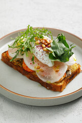 Toast with grilled shrimps and vegetables, poached egg and herbs on top served in restaurant.