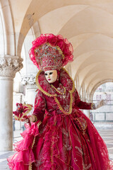 Fototapeta na wymiar donna in costume di carnevale rosso, inserita in un sottoportico di palazzo ducale, figura intera, bouquet nella mano sinistra