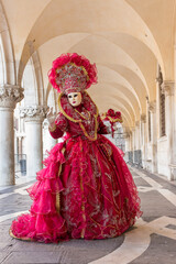 Fototapeta na wymiar donna in costume di carnevale rosso, inserita in un sottoportico di palazzo ducale, figura intera, bouquet nella mano sinistra
