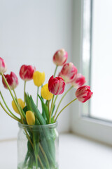 Indoors, selective focus on a bouquet of fresh tulips that stand on the window in a glass jar, copy space.