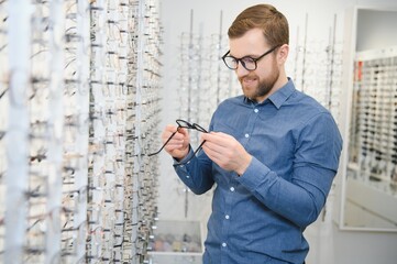 Shot of a handsome bearded man trying on new glasses at the eyewear store.Man buying...