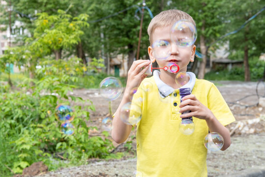 Happy little boy have fun blowing colorful shiny rainbow bubbles outdoors in the garden, summertime