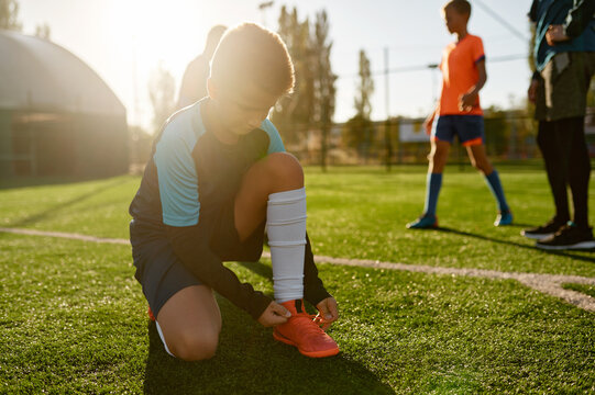 Closeup boy little football player tying shoelaces sitting on soccer field