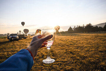 hand holding a wine glass in front of of sunrise with hot air balloons rising over fields and ancient teotihuacán ruins outside of Mexico City