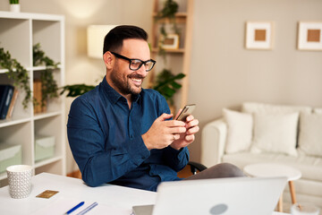 Young smiling man is using a smartphone in home office