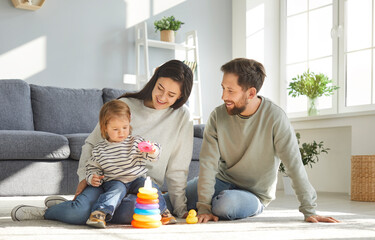 Caucasian family with their little daughter builds rainbow tower while playing on floor of...