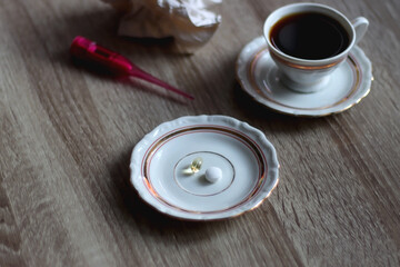 Cup of tea, pills, pink thermometer and used tissue on the table. Cold and flu concept. Selective focus.