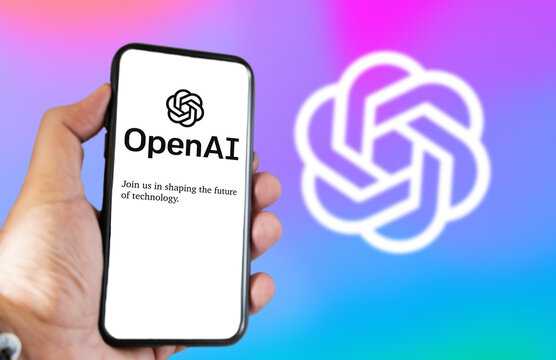 A hand holding a phone with the OpenAI website on the screen