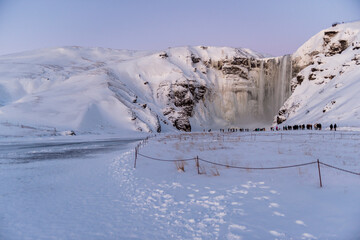 imagen de  la cascada de Skógafoss con el entorno nevado, y una capa de hielo cubriendo el río....