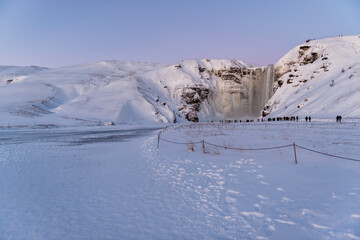 imagen de  la cascada de Skógafoss con el entorno nevado, y una capa de hielo cubriendo el río....