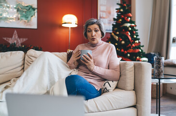 Senior woman with cup of hot drink sitting on sofa
