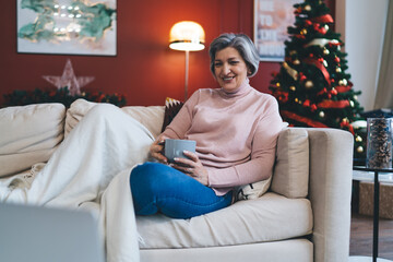 Obraz na płótnie Canvas Senior woman with cup of hot drink sitting on sofa