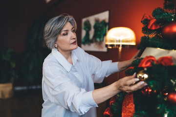 Aged gray haired woman hanging golden bauble on Christmas tree
