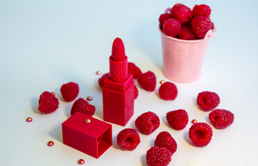 Bright red lipstick and ripe juicy raspberries on white background.