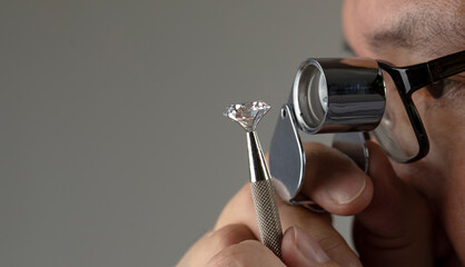 Diamond dealer evaluates the quality of round cut diamond through magnifying glass. High quality...