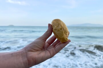 a man's hand holds a piece of bad-smelling ripe durian against the background of the sea, ocean, water in a tropical country
