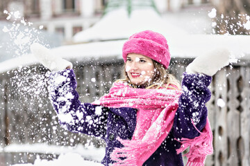 Portrait of a smiling young woman in a bright pink scarf and hat, white mittens and a purple fur...