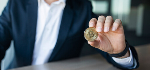 Closeup shot of businessman showing bitcoin, sitting at workplace in office, selective focus, panorama, copy space