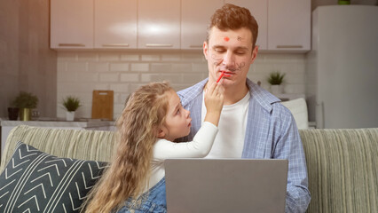 Preschooler girl enjoys painting with red lipstick father lips. Concentrated freelancer tries to...