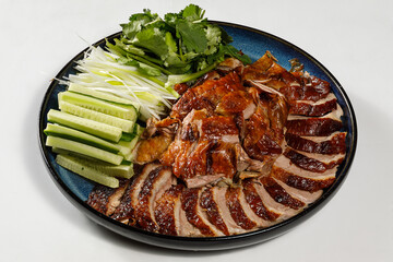 Peking Duck on the plate served with fresh cucumber, green onions, cilantro and roasted wheaten chinese pancakes with sauce Hoysin on white background
