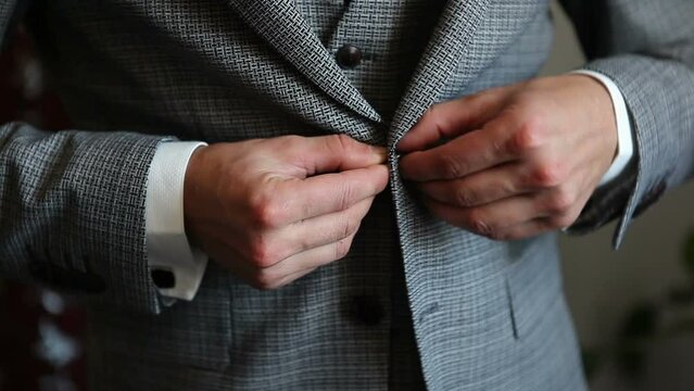 An elegant young man in a suit fastens a button on his jacket.
