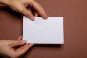 two female hands holding a blank piece of paper with copy space in front of a brown colored background cardboard