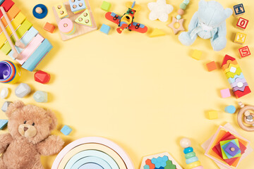 Fototapeta na wymiar Baby kids toy frame background. Teddy bear, colorful wooden educational, musical, sensory, sorting and stacking toys for children on yellow background. Top view, flat lay