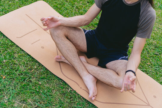 High angle of a young male yogi sitting on a yoga mat in lotus pose doing the shuni mudra on the grass.
