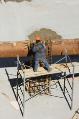builder in orange helmet works, construction of multi-storey building or shopping center in city. modern architecture work on building object. monolithic skyscraper metal fittings, technologies