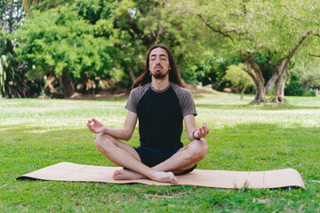 Young Latino and Hispanic hippie man with long hair and beard practicing yoga doing the lotus pose...