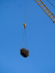 Tower crane lifts metal rebar. The load is suspended on a crane hook against a blue sky. Birds are...