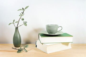 Wooden desk or table with books, a green tea cup and sage twigs in a small ceramic vase against a...