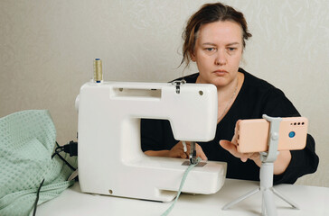 A female seamstress sews green fabric items on a sewing machine.