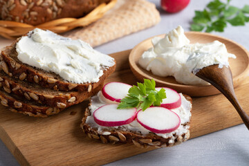 Home made rye bread on a wooden cutting board with curd cheese, radish and ricotta and herbs....
