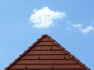 Red brown clay tile sloped pitched roof. blue sky and white clouds. metal snow breakers. ridge...