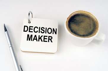 On a white surface, a cup of coffee, a pen and a notepad with the inscription - DECISION MAKER