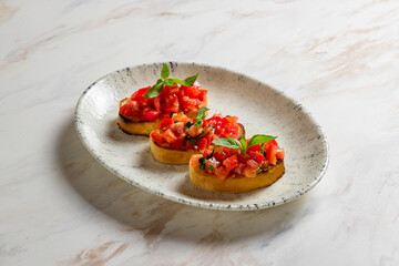 bruschetta with sliced tomatoes cubes and basil on plate on marble table