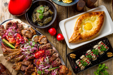 platter of different kebabs, Adjara khachapuri, dolma and auberdine eggplant rolls with nuts on wooden table top view