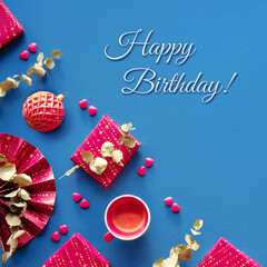Happy birthday in wintertime, December, January, February. Magenta gift boxes, paper fan, eucalyptus, sugar hearts. Square geometric corner composition, flat lay on dark blue textile linen background.