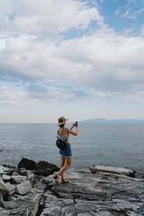 Woman traveler, backpacker, taking pictures with smartphone, while exploring Greek sea