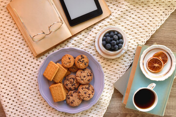 Plate of cookies, cup of tea, fresh blueberries, dry oranges, stack of books, reading glasses and tablet on the table. Hygge at home. Flat lay.